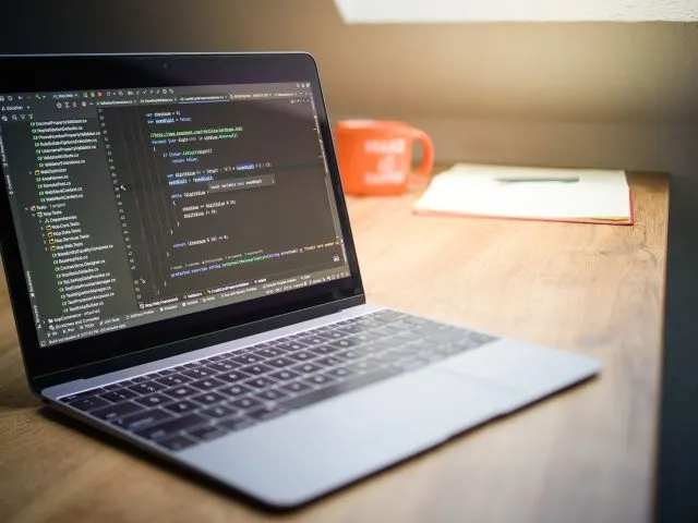 Developer's laptop showing code on a wooden desk, representing a bespoke custom website rebuild